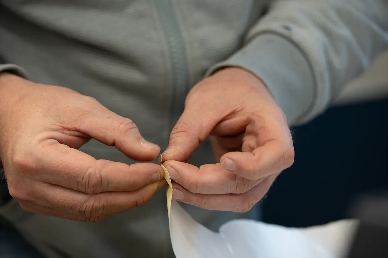 Hände ziehen Klebeetikett von weißer Rückseite ab.